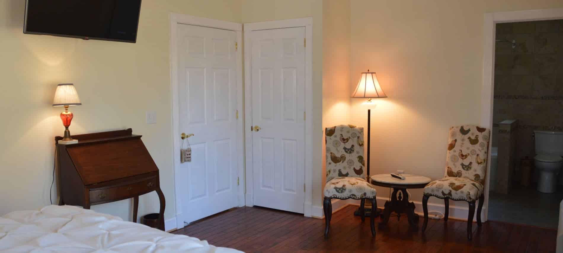 Bedroom with white bedding, sitting area, flat-screen tv mounted on the wall, hardwood floors, and yellow walls