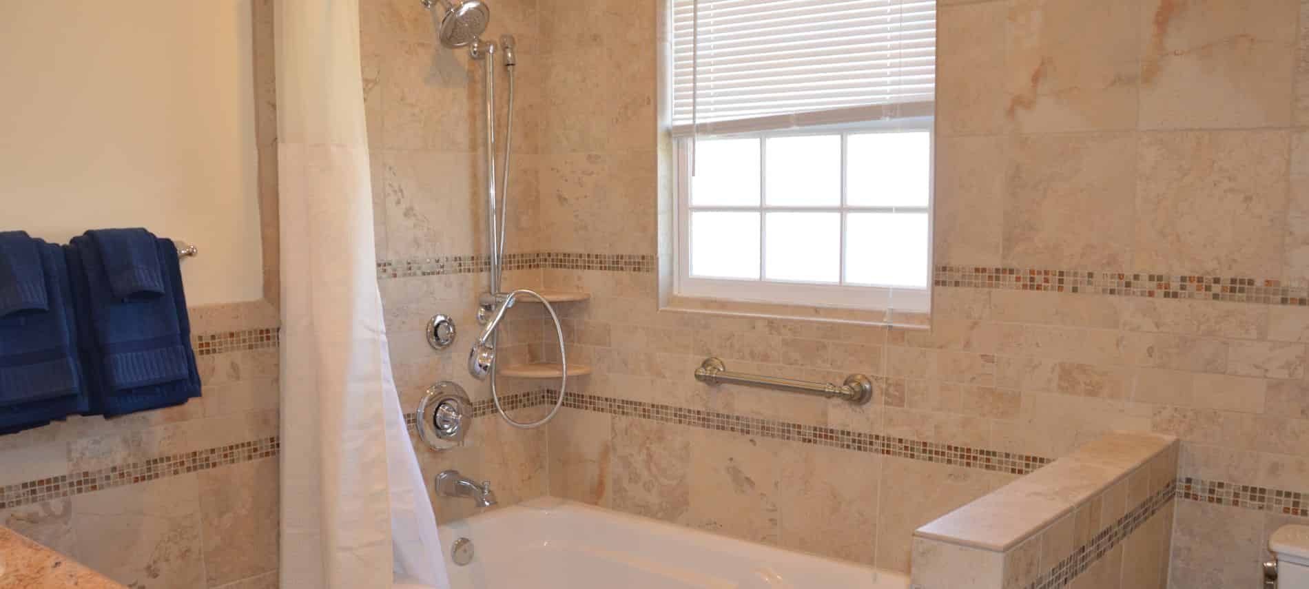 Bathroom with light brown and cream tiled walls, white tub, white shower curtain, and navy towels