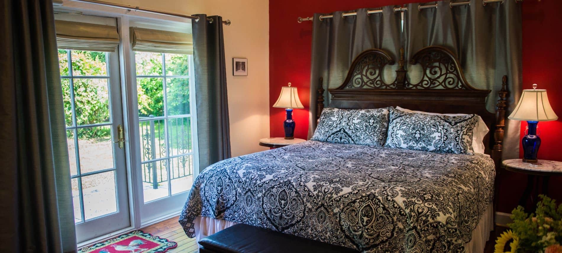 Bedroom with dark wooden ornate headboard, black and white bedding, hardwood floors, and dark red accent wall