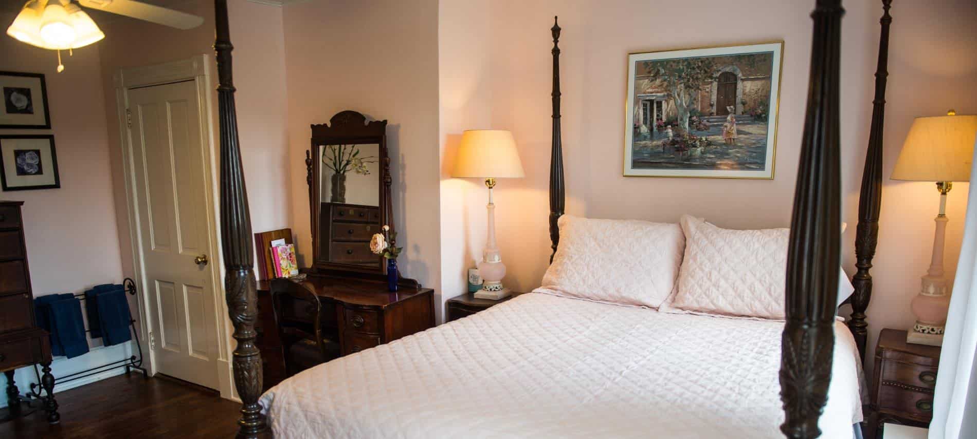 Bedroom with dark wooden furniture, four-post bed, light pink bedding, hardwood floors, and light pink walls