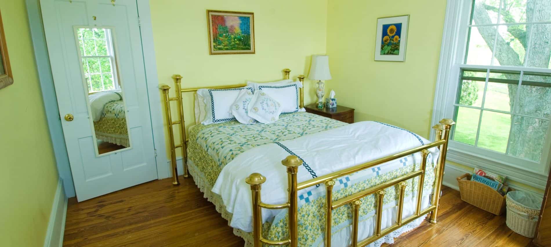Bedroom with golden brass headboard and footboard, green, blue, and yellow floral quilt, hardwood floors, and yellow walls