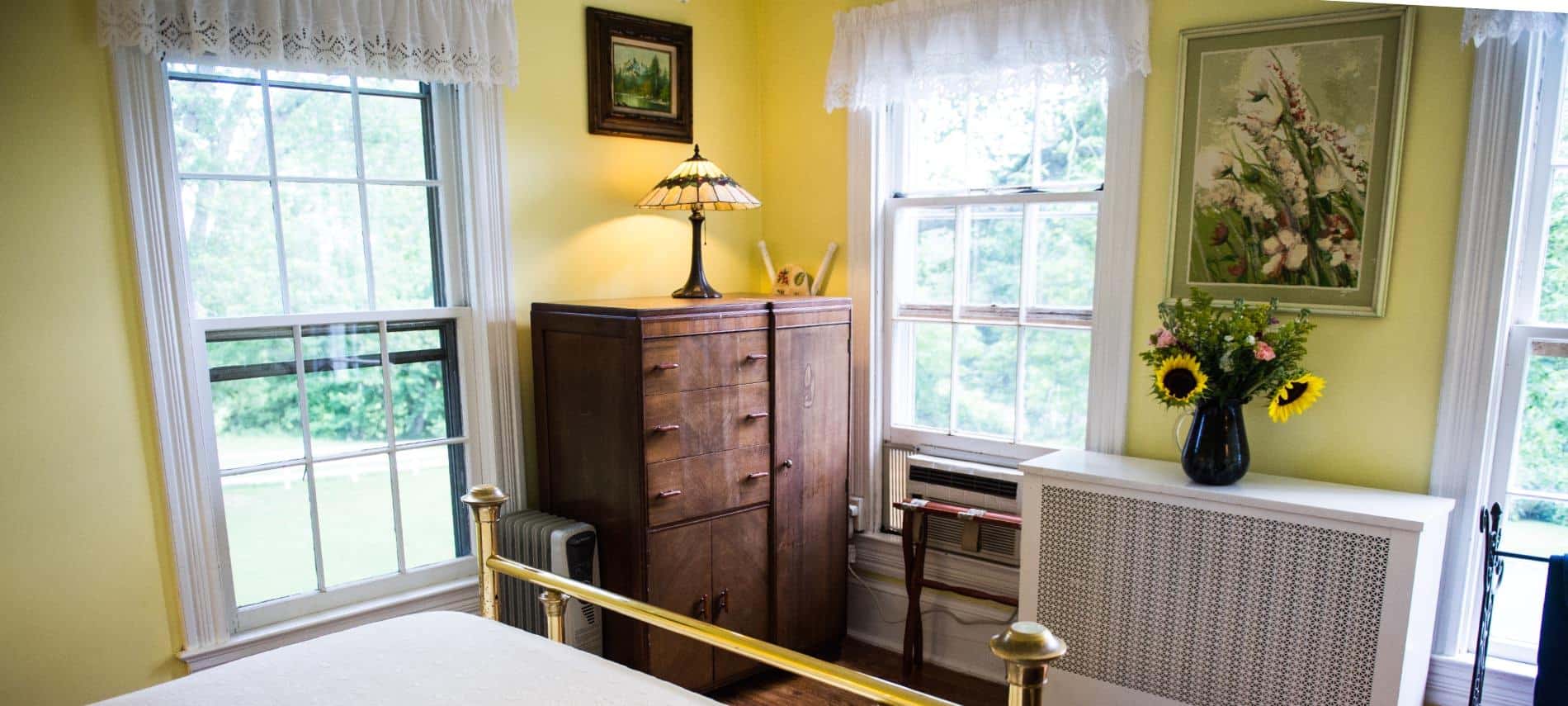 Bedroom with golden brass footboard, white bedding, hardwood floors, and yellow walls