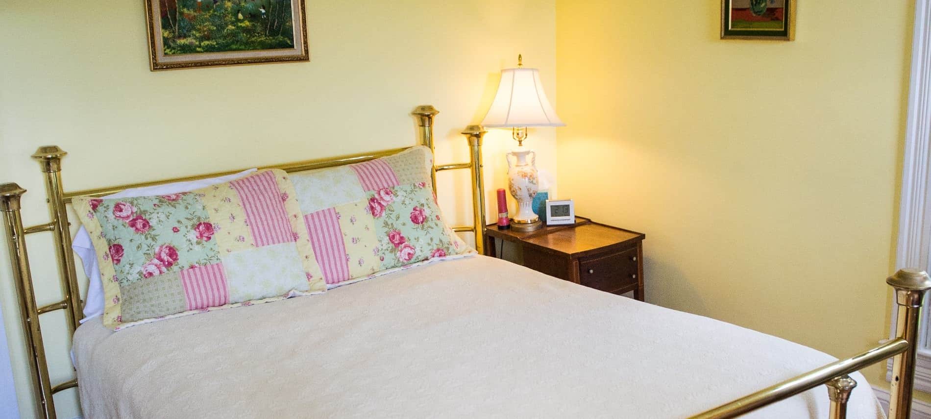 Bedroom with golden brass headboard and footboard, cream quilt, hardwood floors, and yellow walls