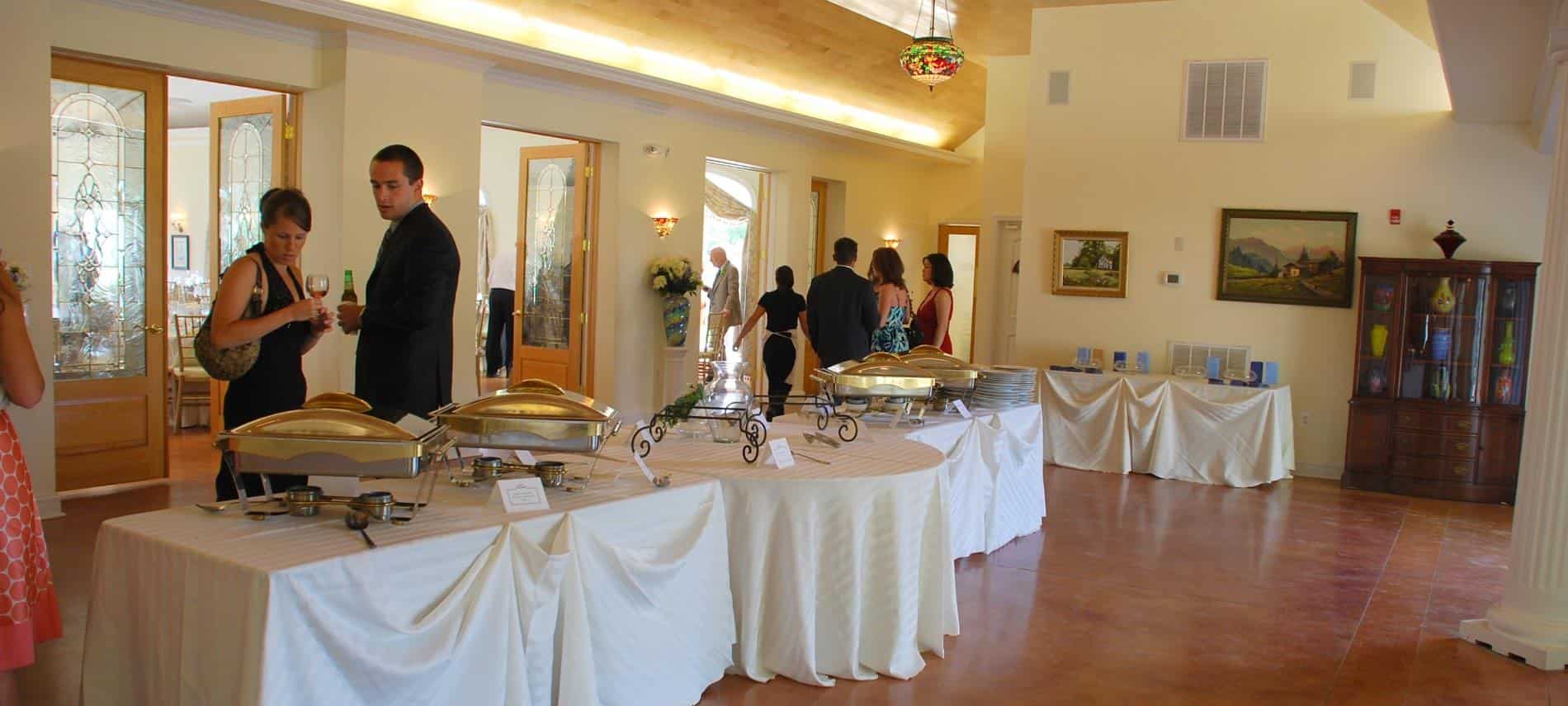 Large room with tables covered with white tablecloths and set up for a dinner buffet