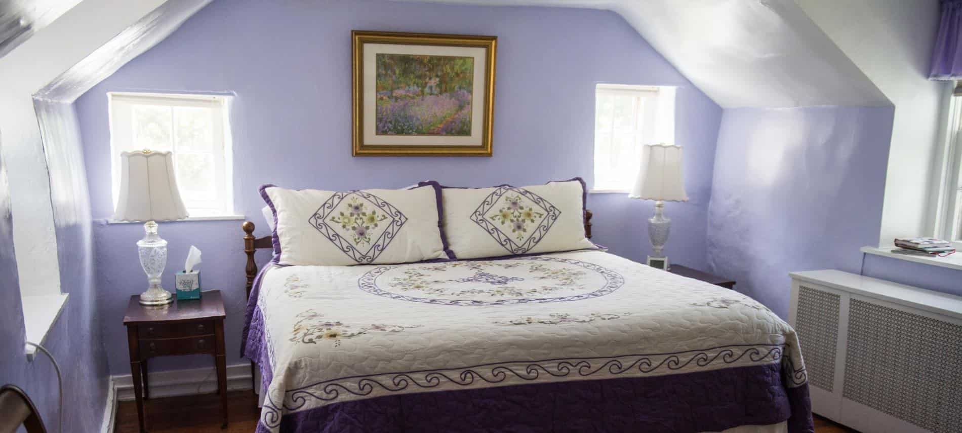 Bedroom with dark wood furniture, dark purple and white bedding, hardwood floors, and light purple walls