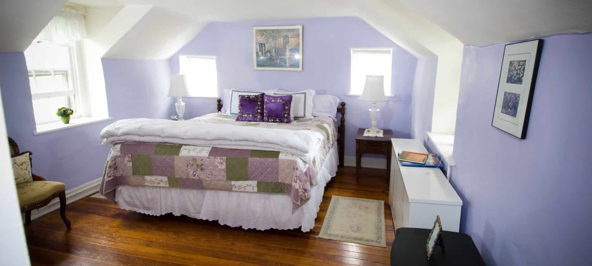 Bedroom with dark wood furniture, green, violet, tan, and white bedding, hardwood floors, and light purple walls