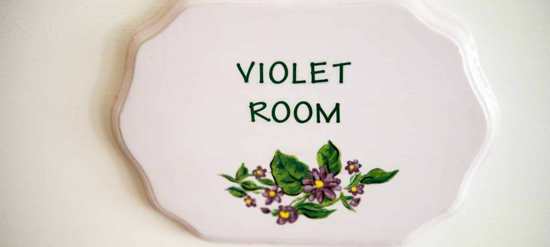 Wooden plaque painted white with purple flowers and green leaves and the words Violet Room