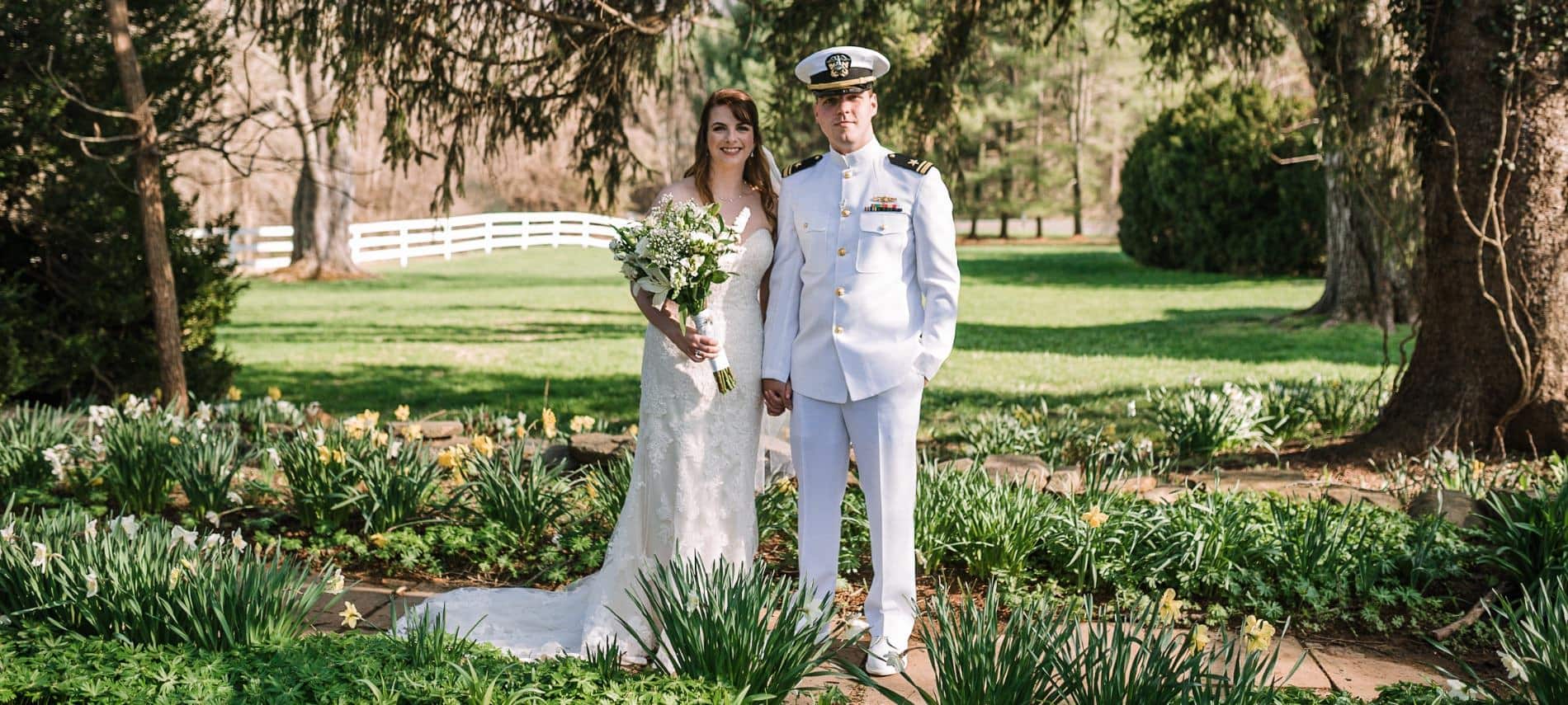 Bride in white wedding dress and groom in white naval uniform standing near yellow and white flowers