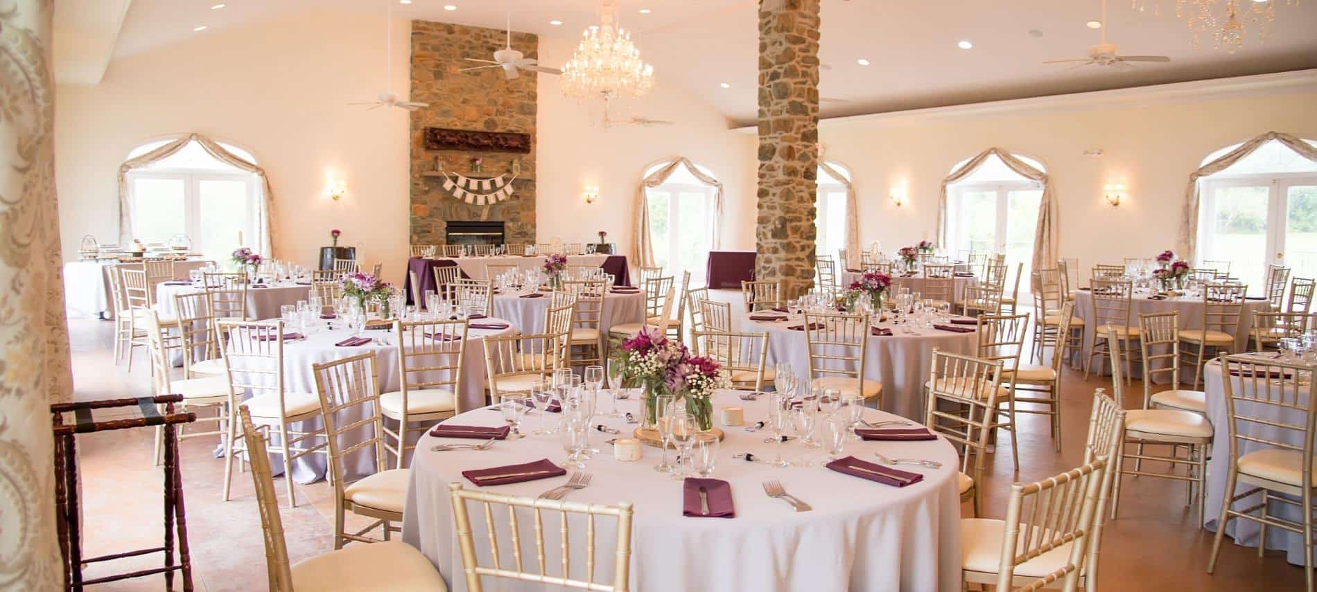 Large room decorated for a wedding reception with white tablecloths and burgundy napkins