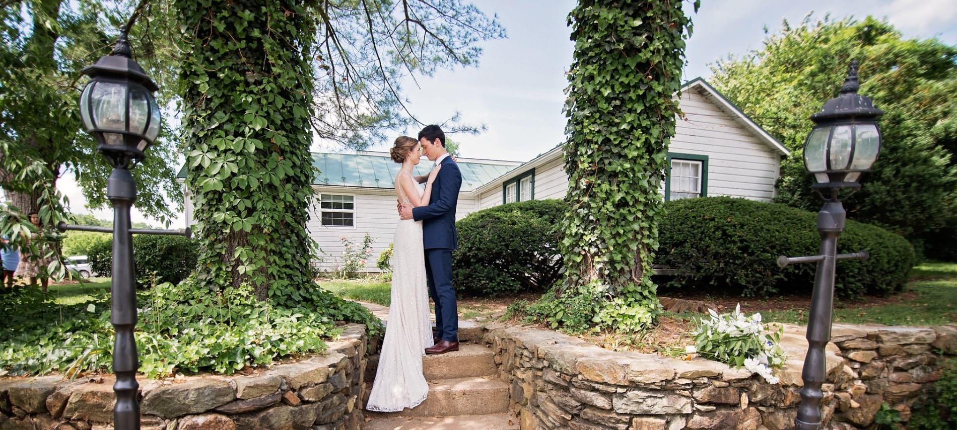 Bride in white dress and groom in dark blue suit standing close to each other on steps in front of cottage